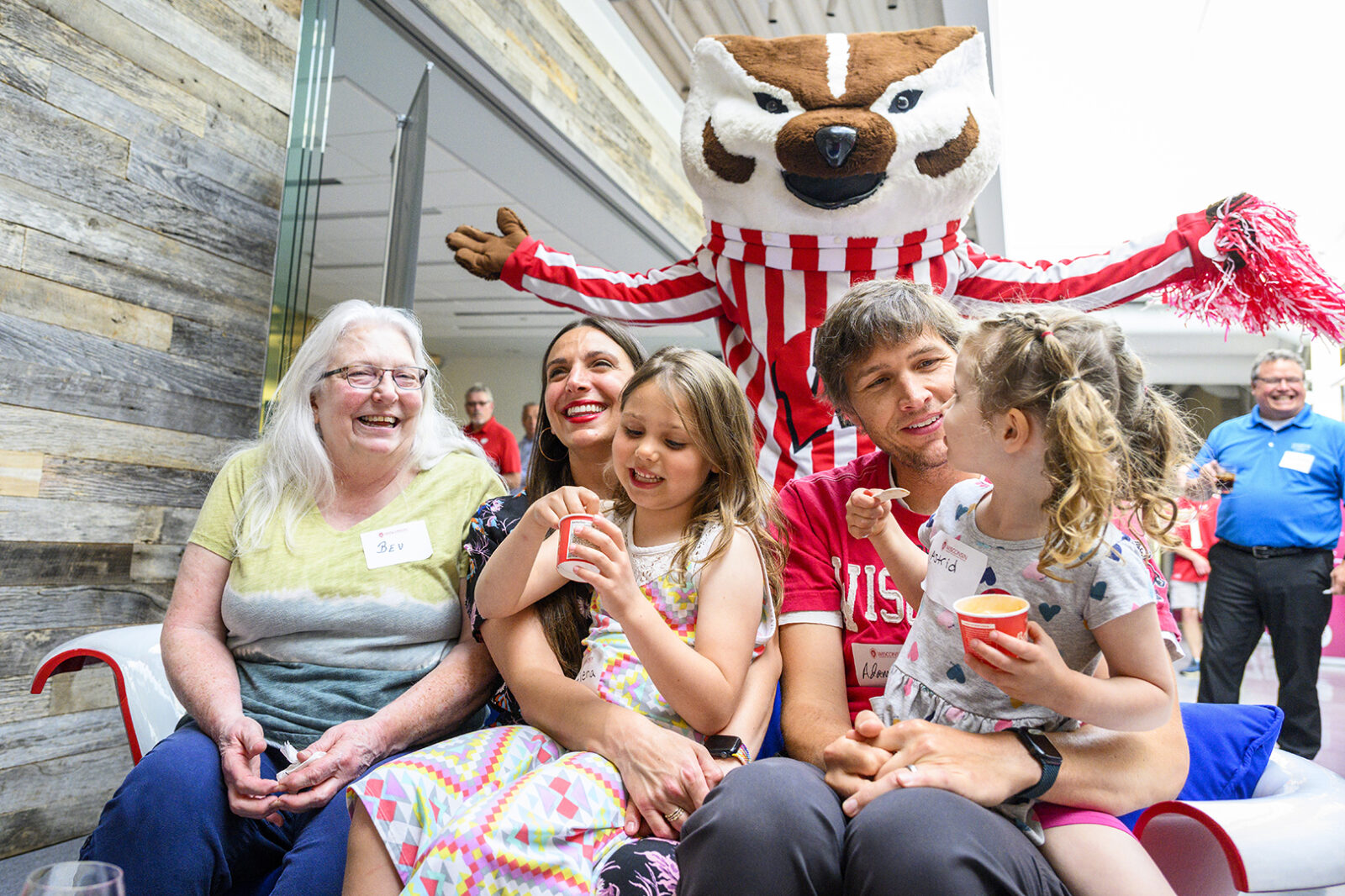 A candid photo of a family sitting and enjoying ice cream while Bucky Badger poses behind them